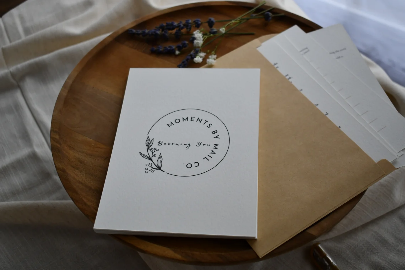 Becoming You card and envelope arranged with dried flowers on a wooden tray.