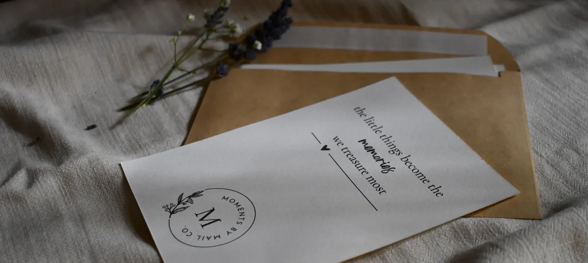 A Moments by Mail Co. note card resting on an envelope with small flowers.