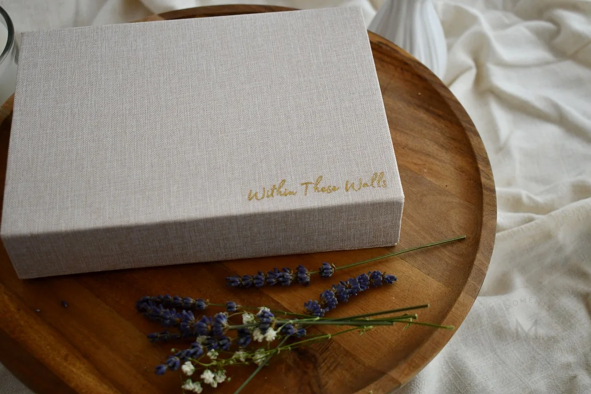 Within These Walls linen keepsake box on a wooden tray with lavender and white flowers.