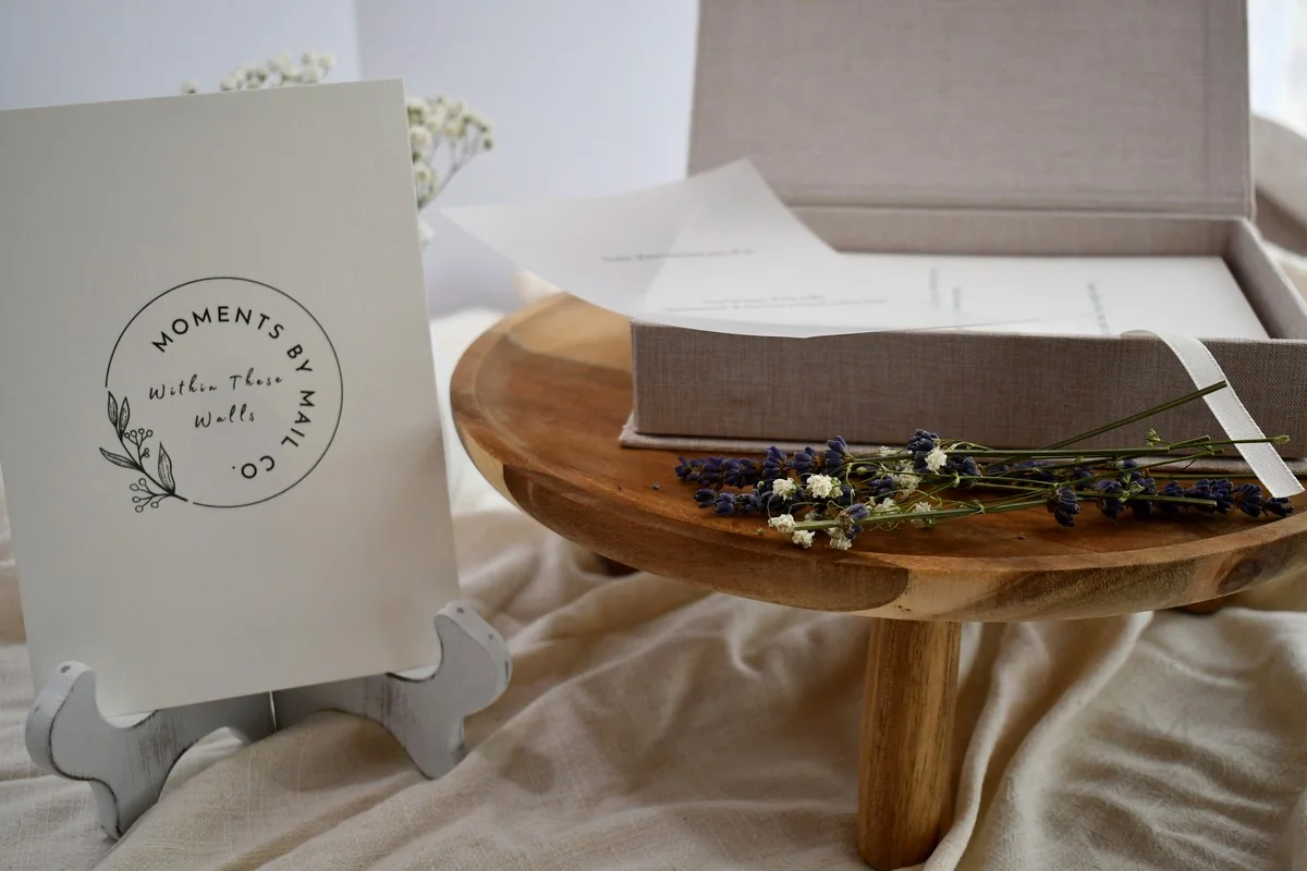 Within These Walls keepsake card beside an open linen box styled with flowers.